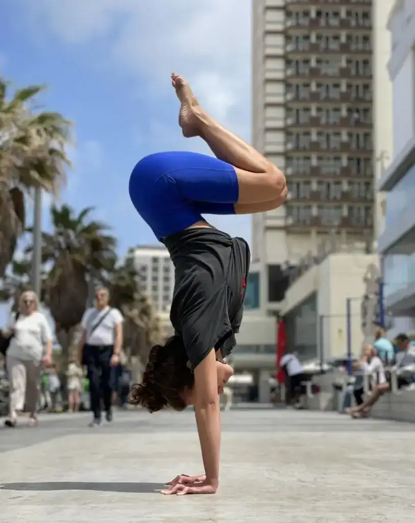 מתאמנת מבצעת עמידת ידיים בחוף הים של תל אביב